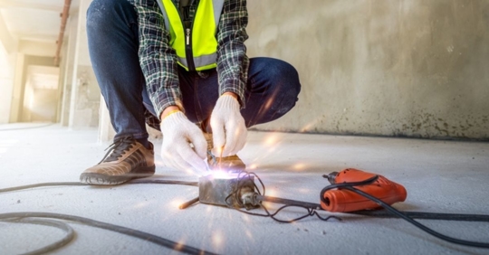 close up of a construction worker holding wires near a sparking electrical outlet