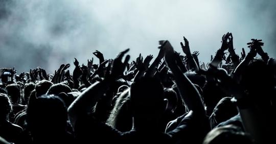 image of the top of a crowd with their hands up and smoke in the air