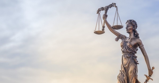 blind justice statue positioned with a sky in the background