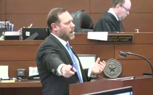 Attorney Michael Lyons standing at a court room podium pointing to the defendants table